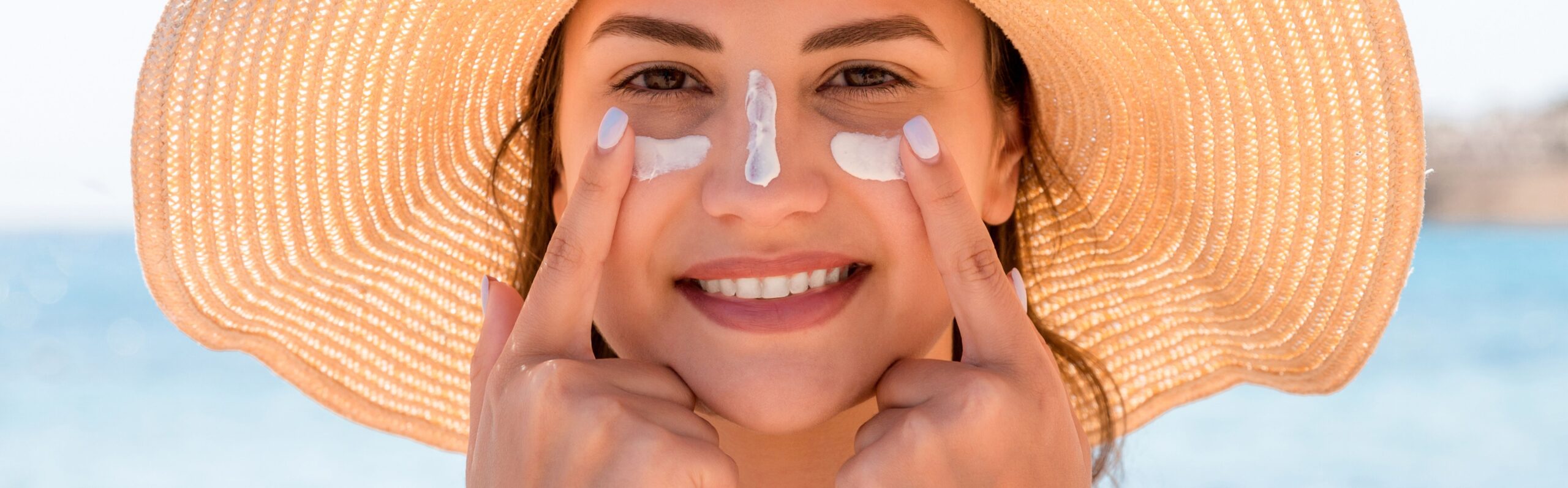 Woman smiling while applying sunscreen with UV filters to her face